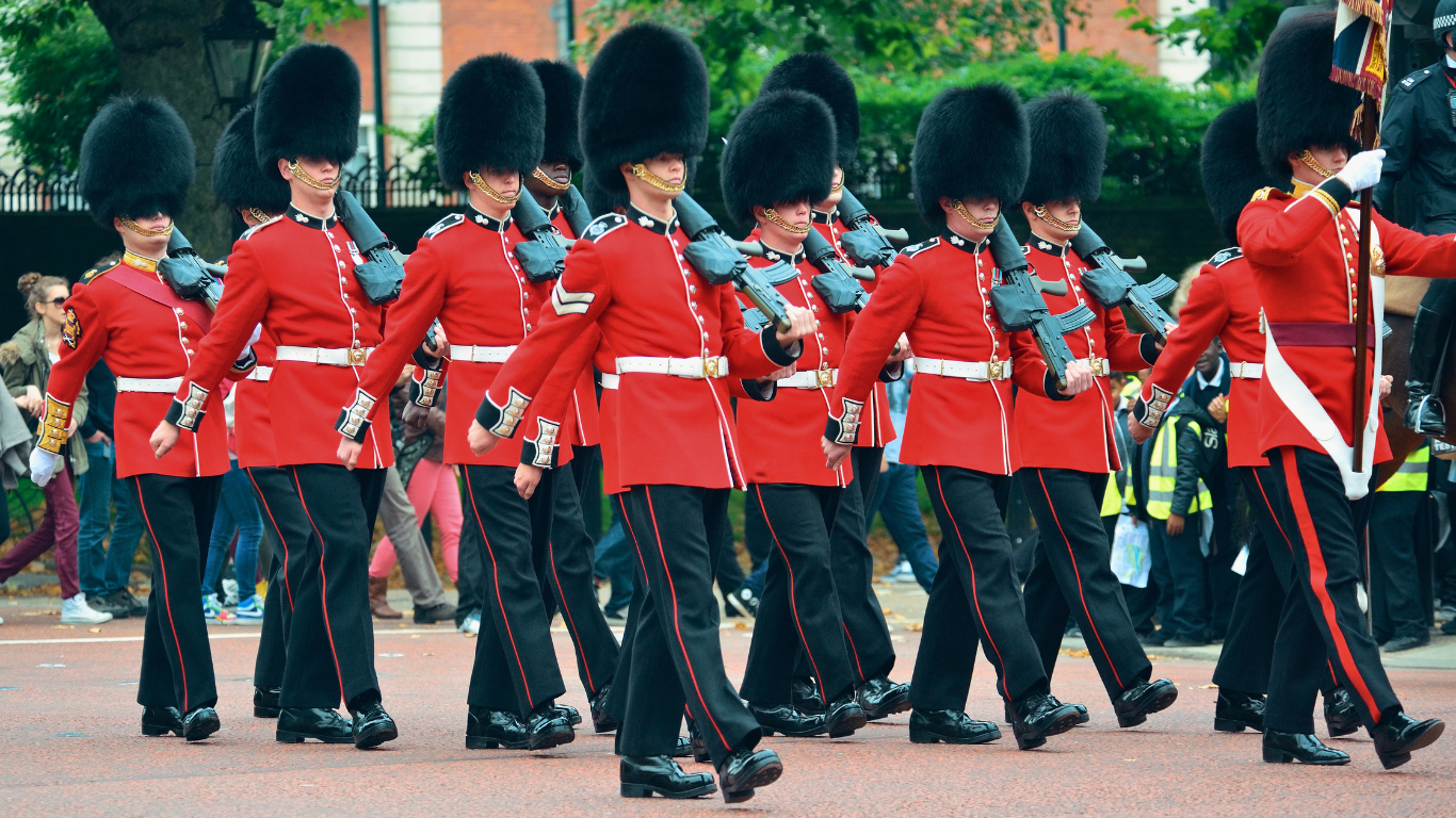 Groupe de soldats en uniforme rouge et bleu, coiffés de bonnets noirs, marchant en formation dans la rue.