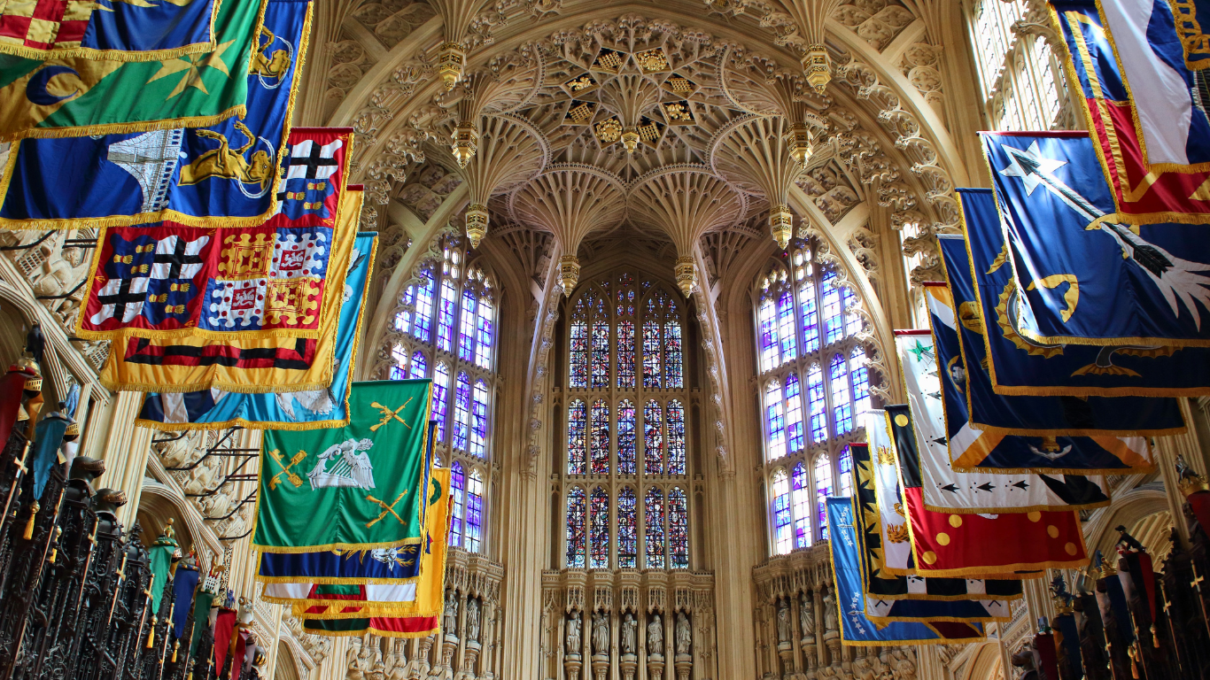 Intérieur d’une cathédrale gothique, hautes fenêtres et drapeaux colorés suspendus sous une voûte sculptée.
