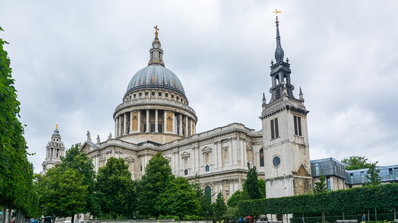 Cathédrale Saint-Paul de Londres avec dôme doré, clocher et verdure, ciel nuageux.