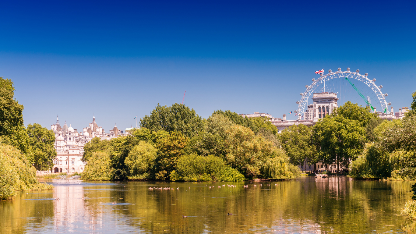 Vue du lac avec arbres verts, et la grande roue de Londres au loin sous ciel bleu.