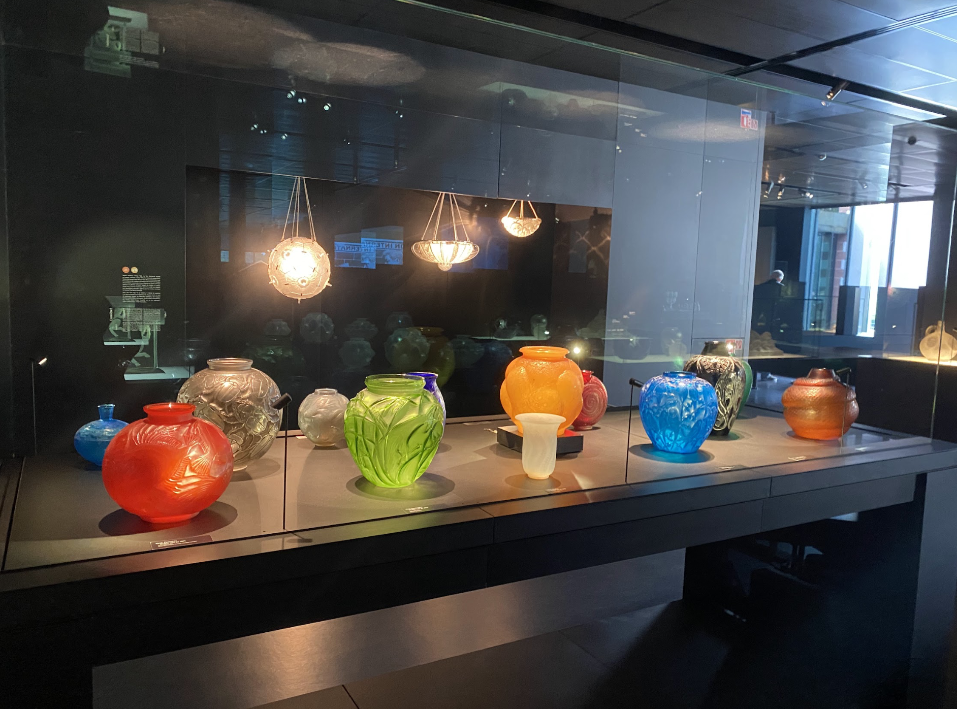 Vitrine du parcours permanent du Musée Lalique (Wingen-sur-Moder) contenant des vases en verre. De gauche à droite : vase Poissons (rouge), vase Sauterelles (vert), vase Tortue (orange), vase aux Perruches (bleu), vase Serpent (orange). CC0