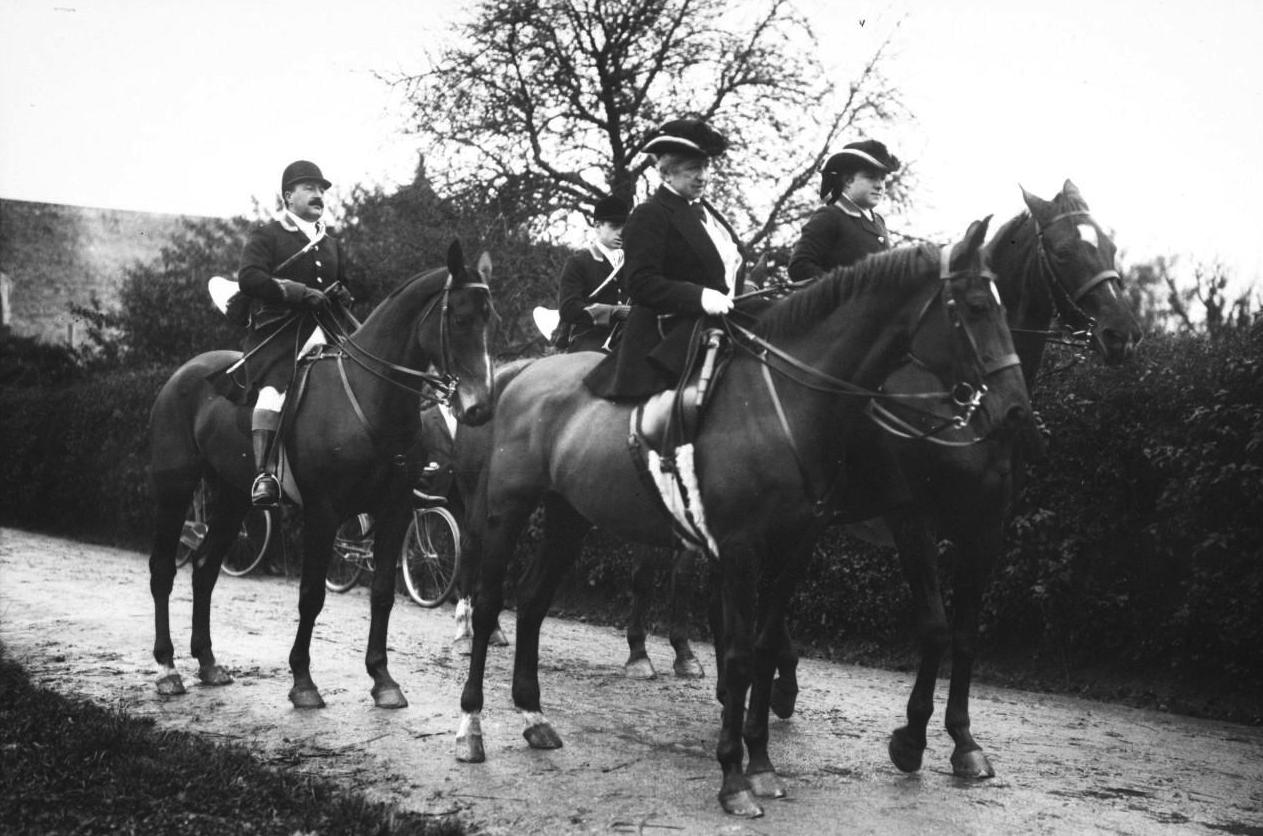 Cavalier en uniforme à cheval, plusieurs hommes à la promenade équestre sur un chemin rural, arbres en arrière-plan.
