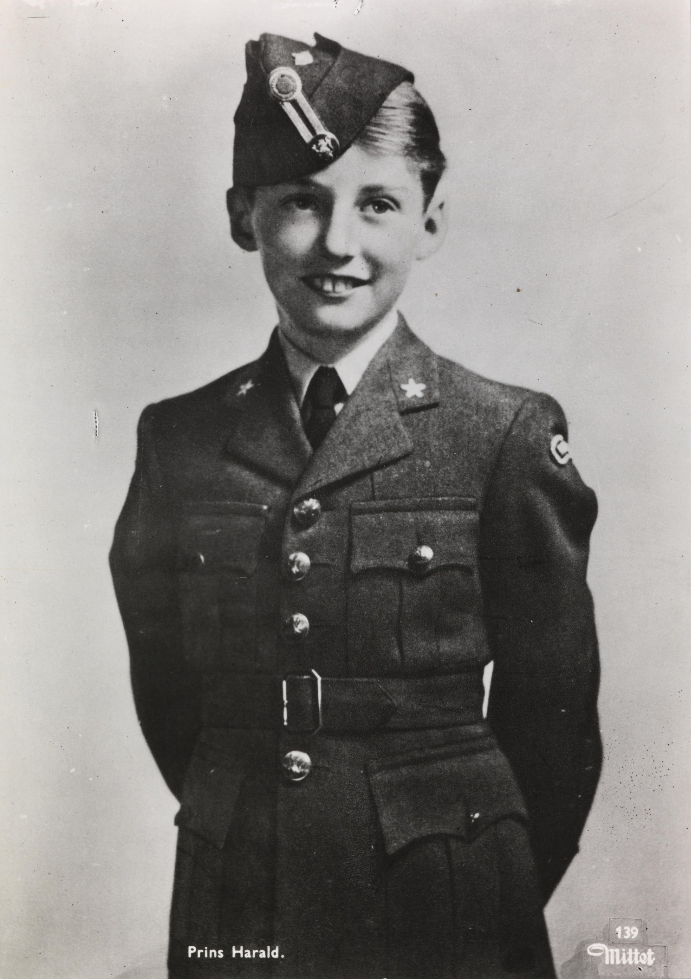 Portrait noir et blanc d’un homme en uniforme, chapeau à insigne, sourire, buste en studio.